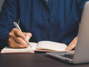 A man participates in virtual life skills coaching and writes down notes in his notebook.