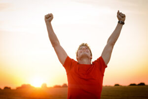 A man smiles and lifts his arms up in victory after overcoming challenges in recovery.